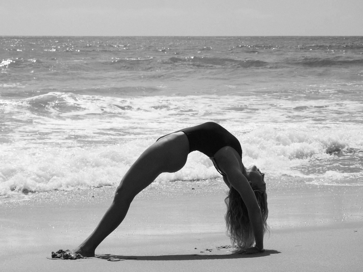 Black and white photo of Macy in a backbend at the shoreline