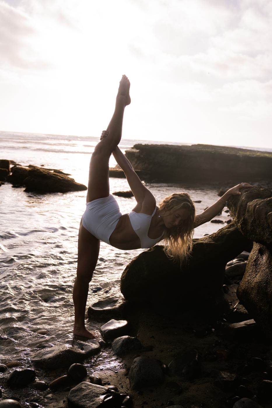 Macy in a standing split against the rocks at sunset